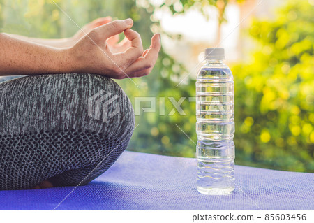 hand of a woman meditating in a yoga pose on a rug for yoga and a bottle of water hand of a woman meditating in a yoga pose on a rug for yoga and a bottle of water 85603456