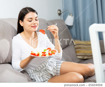 Woman eating salad on sofa 85604008