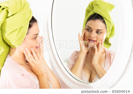 Woman with towel on his head near mirror and touching face Woman with towel on his head near mirror and touching face 85604014