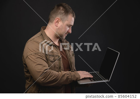 Middle aged Caucasian man uses laptop while standing in studio. Portrait of a freelancer surfing the internet 85604152