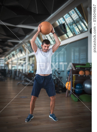 Man exercising in the gym with a heavy medicine slam ball Man exercising in the gym with a heavy medicine slam ball 85604667