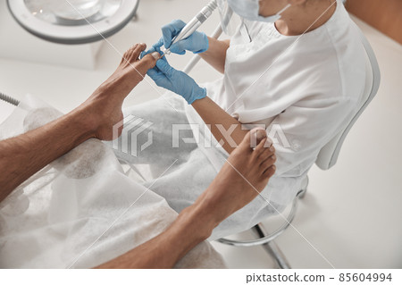 Lady uses grinding machine to polish toenail of male client at in beauty salon Lady uses grinding machine to polish toenail of male client at in beauty salon 85604994