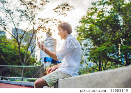 Young Man on the phone. Dressing in a white shirt, beige shorts. Mobile Office concept Young Man on the phone. Dressing in a white shirt, beige shorts. Mobile Office concept 85605149