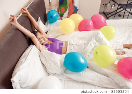 Happy young woman lying in bed with colorful balloons 85605204