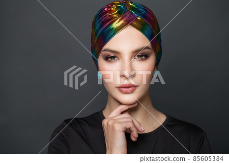 Beautiful stylish woman wearing a headscarf turban and touching her chin while looking at camera Beautiful stylish woman wearing a headscarf turban and touching her chin while looking at camera 85605384