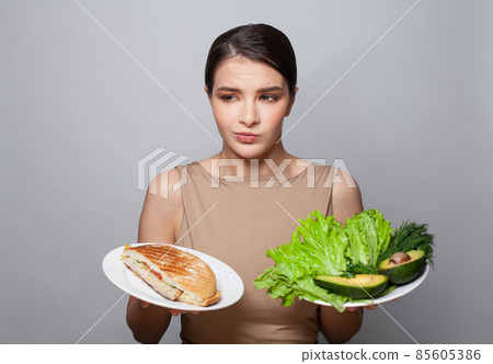 Studio shot of a young brunette woman choosing between healthy and unhealthy foods Studio shot of a young brunette woman choosing between healthy and unhealthy foods 85605386