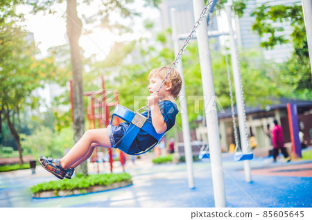 Lovely blond little boy on a swing in the park. Adorable boy having fun at the playground 85605645