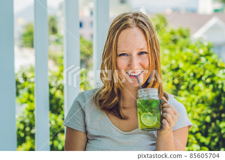 A young woman holds a mason jar in her hand with a mojito. Spring drink concept A young woman holds a mason jar in her hand with a mojito. Spring drink concept 85605704