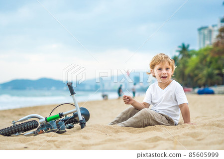 Active blond kid boy and bicycle near the sea. Toddler child dreaming and having fun on warm summer day. outdoors games for children. Balance bike concept 85605999
