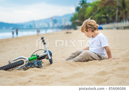Active blond kid boy and bicycle near the sea. Toddler child dreaming and having fun on warm summer day. outdoors games for children. Balance bike concept 85606086