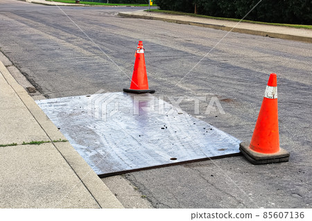 A steel plate on the road with construction pylons 85607136