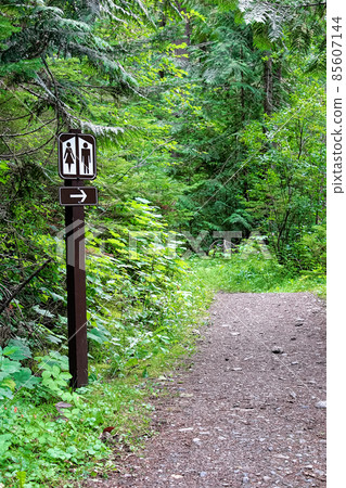 A washroom sign along a path pointing into the forest 85607144