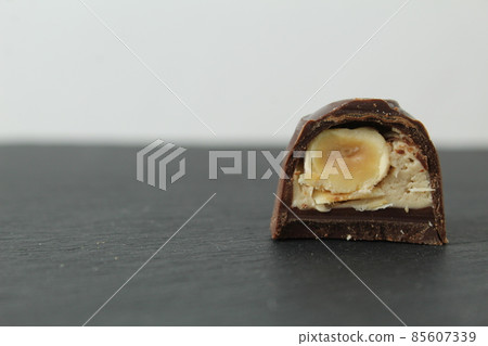 chocolate candy with praline white filling and hazelnut hazelnut in section. Dessert candy lies on a black black background with space for copyspace text. Chocolate Day. Chocolate case candy chocolate candy with praline white filling and hazelnut hazelnut in section. Dessert candy lies on a black black background with space for copyspace text. Chocolate Day. Chocolate case candy 85607339