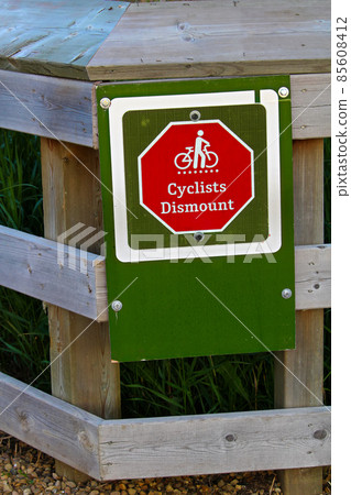 Closeup of a cyclists dismount sign on a fence 85608412