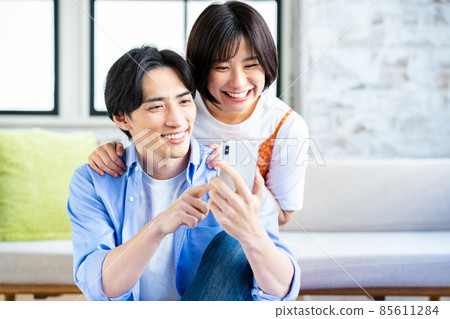一對年輕夫婦在客廳裡看智能手機 一對年輕夫婦在客廳裡看智能手機 85611284