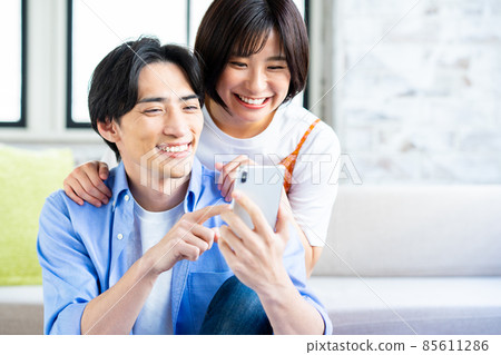 一對年輕夫婦在客廳裡看智能手機 一對年輕夫婦在客廳裡看智能手機 85611286