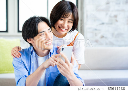一對年輕夫婦在客廳裡看智能手機 85611288