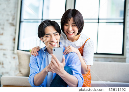 A young couple looking at a smartphone in the living room 85611292