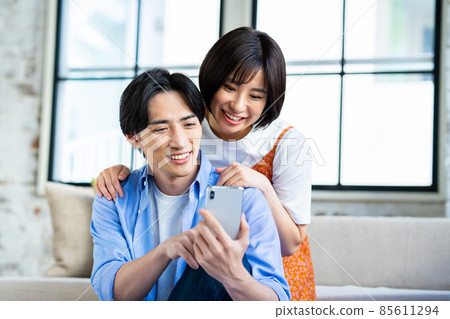 A young couple looking at a smartphone in the living room 85611294