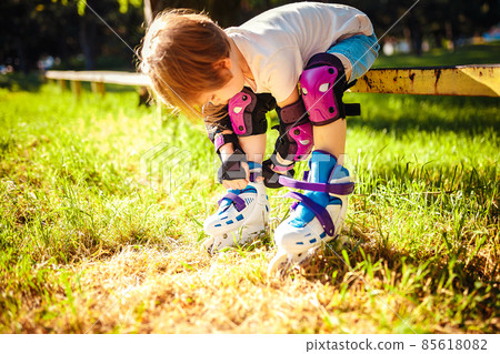 Cute girl dresses roller skates while sitting on the bench. Active healthy lifestyle. safe riding 85618082