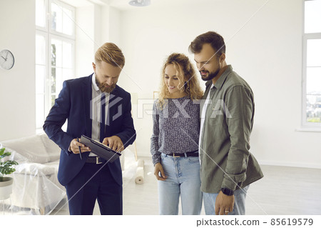 Reaching agreement. Excited young married couple of clients going to sign a deal with a real estate agent during a home inspection. Male realtor explains legal documents to husband and wife. Reaching agreement. Excited young married couple of clients going to sign a deal with a real estate agent during a home inspection. Male realtor explains legal documents to husband and wife. 85619579
