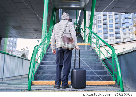 Grey haired pensioner carrying his luggage and looking at the stairs Grey haired pensioner carrying his luggage and looking at the stairs 85620705