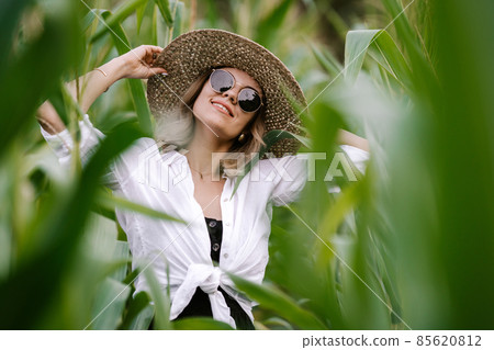 Portrait of young stylish woman in green jungle. Girl in straw hat and sunglasses, linen clothes 85620812
