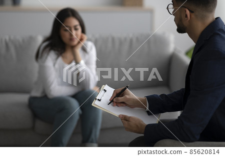 Psychological therapy. Male psychologist noting problems of young arab woman at psychotherapy session, selective focus Psychological therapy. Male psychologist noting problems of young arab woman at psychotherapy session, selective focus 85620814