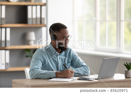 Calm millennial african american male with beard in glasses and headphones watches video lesson on pc Calm millennial african american male with beard in glasses and headphones watches video lesson on pc 85620971