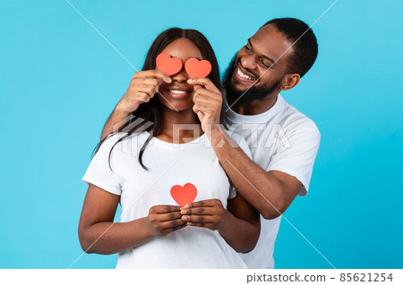 Young Romantic Black Couple Covering Eyes With Red Paper Hearts Young Romantic Black Couple Covering Eyes With Red Paper Hearts 85621254