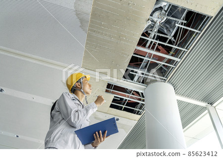 A man in work clothes investigating damaged parts of the building ceiling 85623412