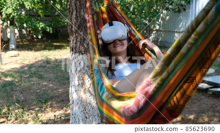 joyful woman wearing virtual reality glasses rests in a hammock near a tree, imagining a dream come joyful woman wearing virtual reality glasses rests in a hammock near a tree, imagining a dream come 85623690