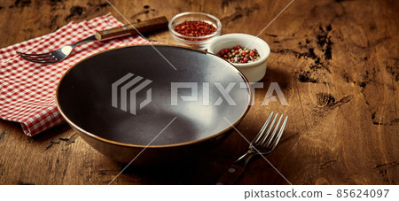 Empty dark bowl with fork, napkin and spices on wooden background 85624097