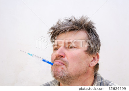 Portrait of a weirdo holding a blue syringe in his mouth. 85624599