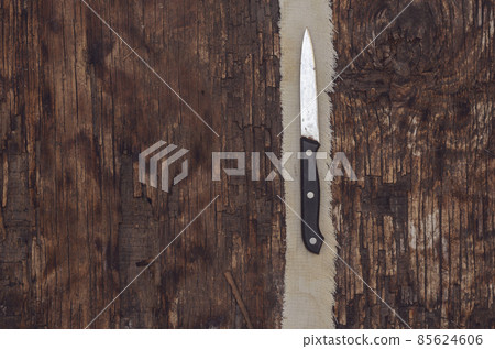 An old kitchen knife and a narrow strip of cloth on a wooden bac 85624606