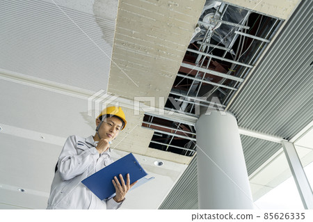 A man in work clothes investigating damaged parts of the building ceiling 85626335