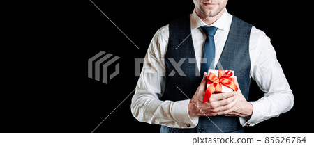 Gift box hand. Happy young business man holding surprise giftbox present with red ribbon isolated on black background. Valentines day, Christmas, New Year banner with copy space. 85626764