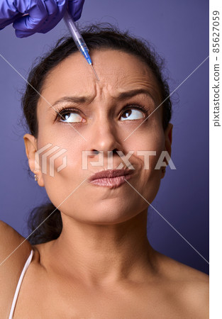 Beautiful middle-aged woman receiving a beauty injection of botulinum toxin into her forehead area to rejuvenate and reduce the signs of ageing and the appearance of the first wrinkles on her face 85627059