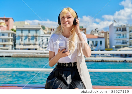 Teenage female in headphones with smartphone on the embankment 85627119