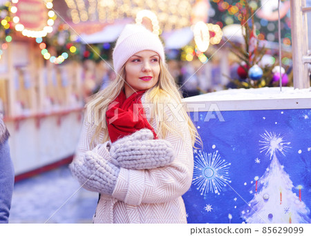 happy blond girl in winter coat and red scarf and knitted mittens blow snow close up portrai 85629099