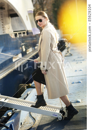 young slavic woman in sun glasses with long hair wearing trench coat boarding on ship for traveling full body photo young slavic woman in sun glasses with long hair wearing trench coat boarding on ship for traveling full body photo 85629104