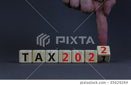 2022 tax new year symbol. Businessman turns a wooden cube and changes words Tax 2021 to Tax 2022. Beautiful grey table, grey background, copy space. Business, 2022 tax new year concept. 2022 tax new year symbol. Businessman turns a wooden cube and changes words Tax 2021 to Tax 2022. Beautiful grey table, grey background, copy space. Business, 2022 tax new year concept. 85629264
