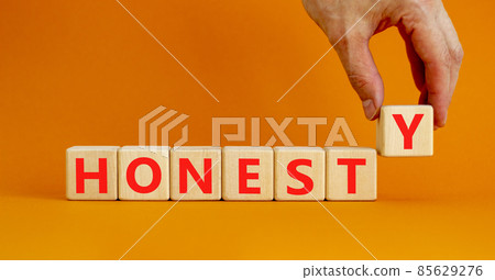 Honesty symbol. The concept word Honesty on wooden cubes. Beautiful orange table, orange background, copy space. Businessman hand. Business and honesty concept. 85629276