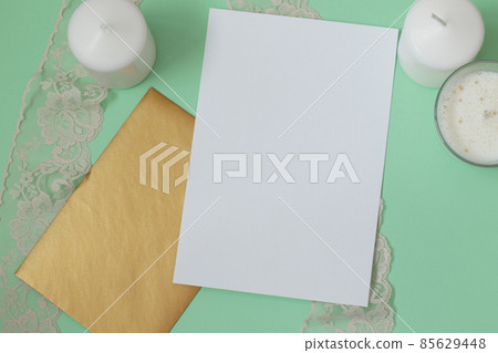 simple invitation mockup with golden envelope, candles and lace on mint green background 85629448