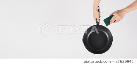 Cleaning Electric non stick pan. Hand on white background cleaning the non stick pan with handy dish washing sponge which yellow color on the soft side and green on hard side for hygiene after cook. 85629945