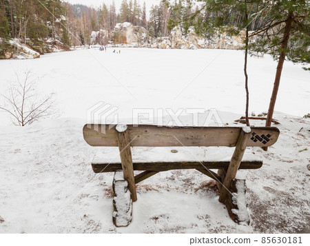 Wooden bench by the frozen blue lake. Winter tracking in popular in Adrspach rocks Wooden bench by the frozen blue lake. Winter tracking in popular in Adrspach rocks 85630181