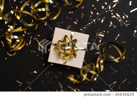 Gift or present box and gold confetti on black table top view. Flat lay composition for christmas, new year , birthday, mother day, black friday , sale, promotions, xmas, or wedding.  85630829