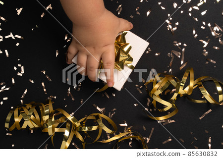 Child's hand opening gift box on black background with gold confetti on black table . Composition for christmas, new year , birthday, mother day, black friday , sale, promotions, xmas, or wedding.  85630832