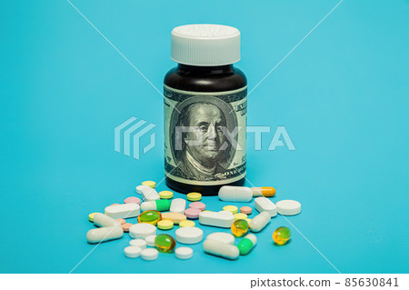 Money and pills of different colors on a blue background. The rise in the cost of medical care. The 85630841