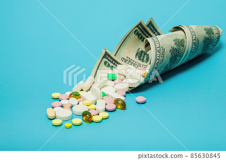 Money and pills of different colors on a blue background. The rise in the cost of medical care. The Money and pills of different colors on a blue background. The rise in the cost of medical care. The 85630845